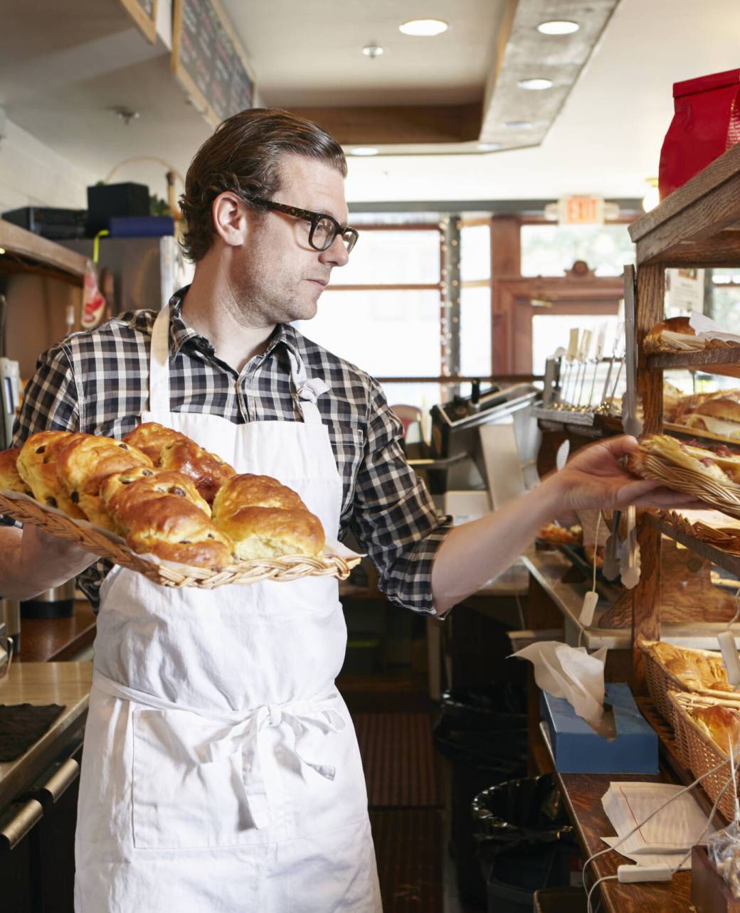 Male worker in bakery, putting fresh pastries into display cabinet